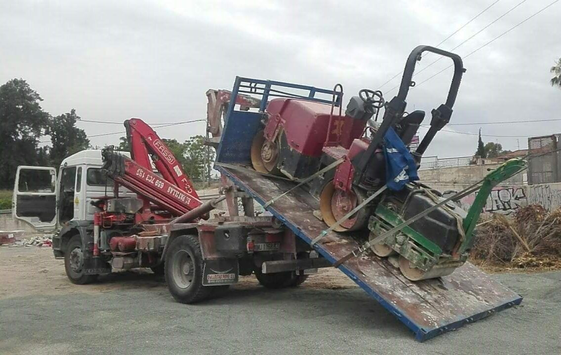 Un camión con una grúa en la parte trasera transporta un tractor.