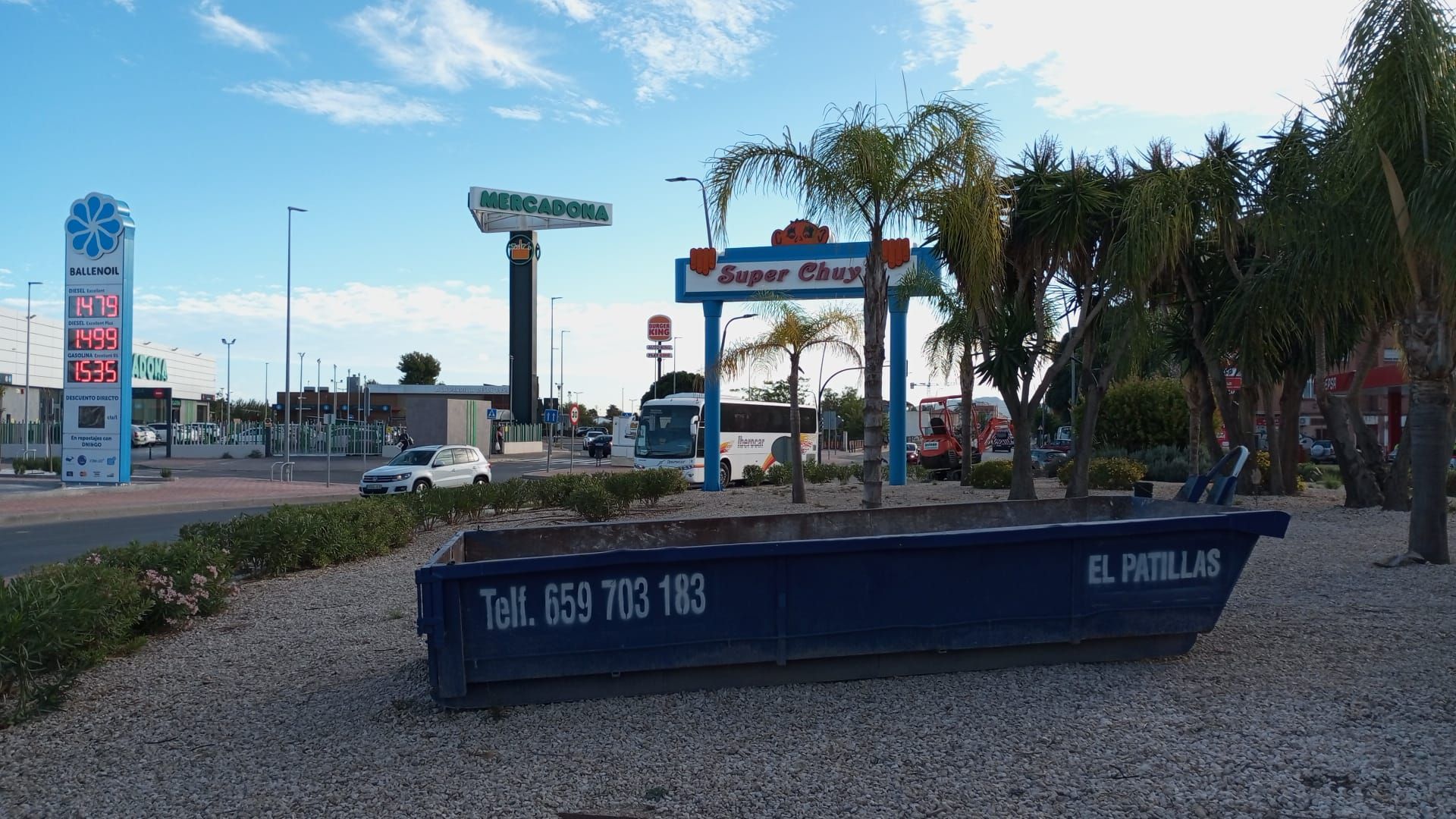 Hay un contenedor de basura delante de una gasolinera.