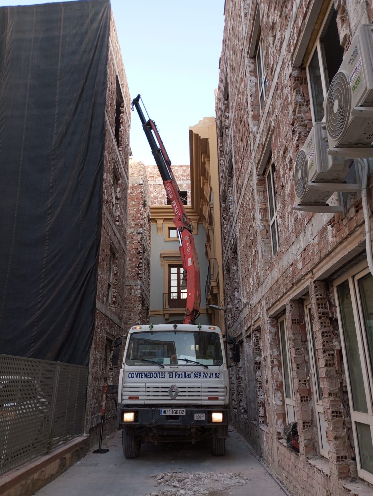 Un camión con una grúa en la parte trasera está estacionado en un callejón estrecho entre dos edificios.