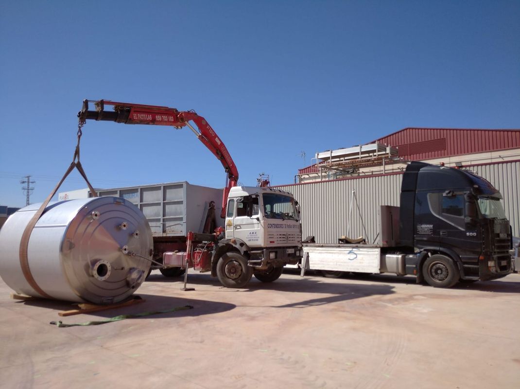 Una grúa está levantando un gran tanque de acero inoxidable desde un camión.