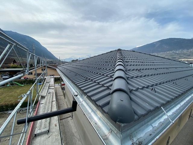 Toiture en construction avec tuiles grises, échafaudages et montagnes en arrière-plan