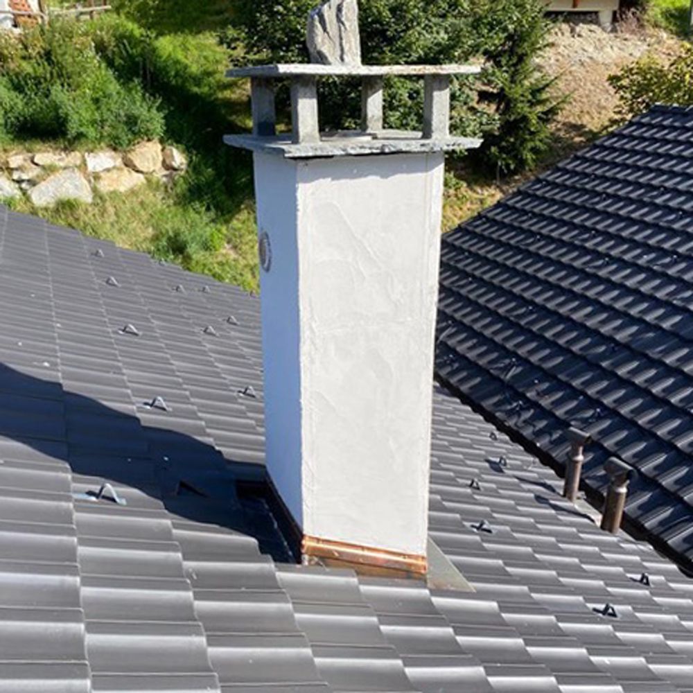 Cheminée blanche s'élevant à travers un toit en métal gris foncé dans un cadre extérieur ensoleillé