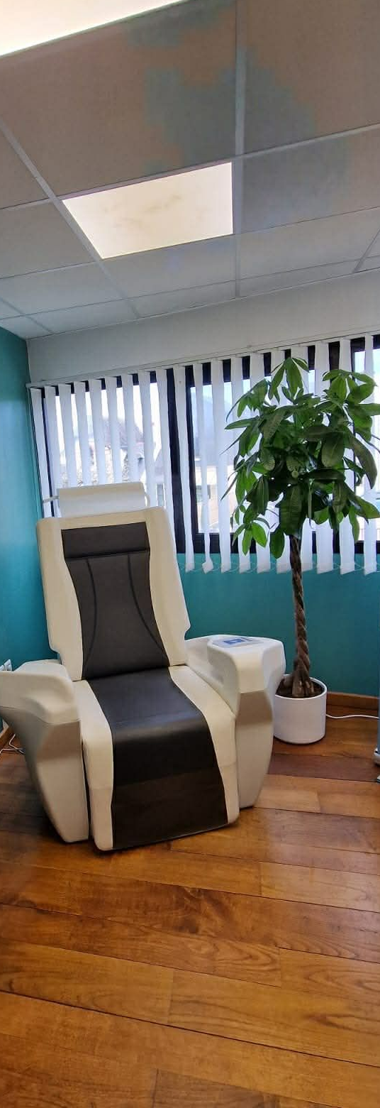 Salle d'exposition avec un fauteuil inclinable gris, un parquet, des bannières publicitaires bleues et une plante en pot.