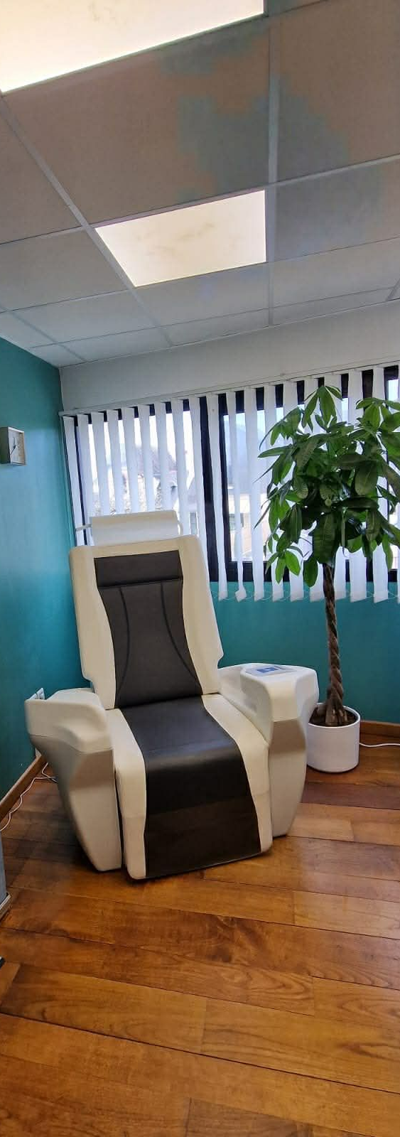 Dans une salle de clinique, un fauteuil spécialisé de thérapie du plancher pelvien, blanc et gris, est placé entre deux bannières publicitaires de marques différentes.