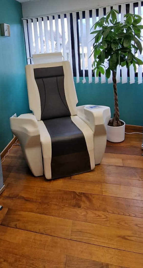 Un fauteuil thérapeutique spécialisé pour le traitement du plancher pelvien est installé dans une pièce, entre deux bannières informatives de marques différentes.