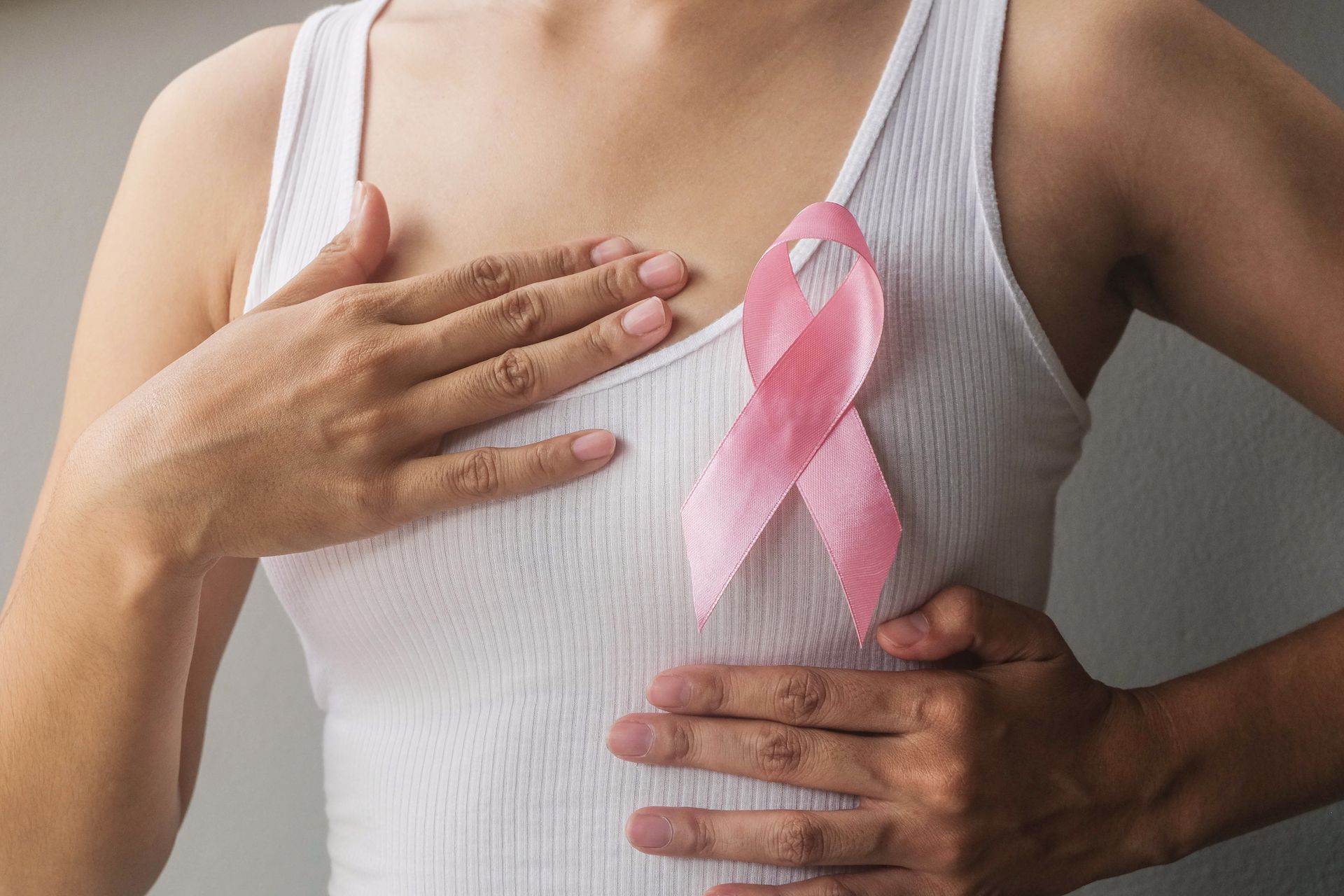 Une personne vêtue d'un débardeur blanc et portant un ruban rose de sensibilisation sur le cancer du sein.
