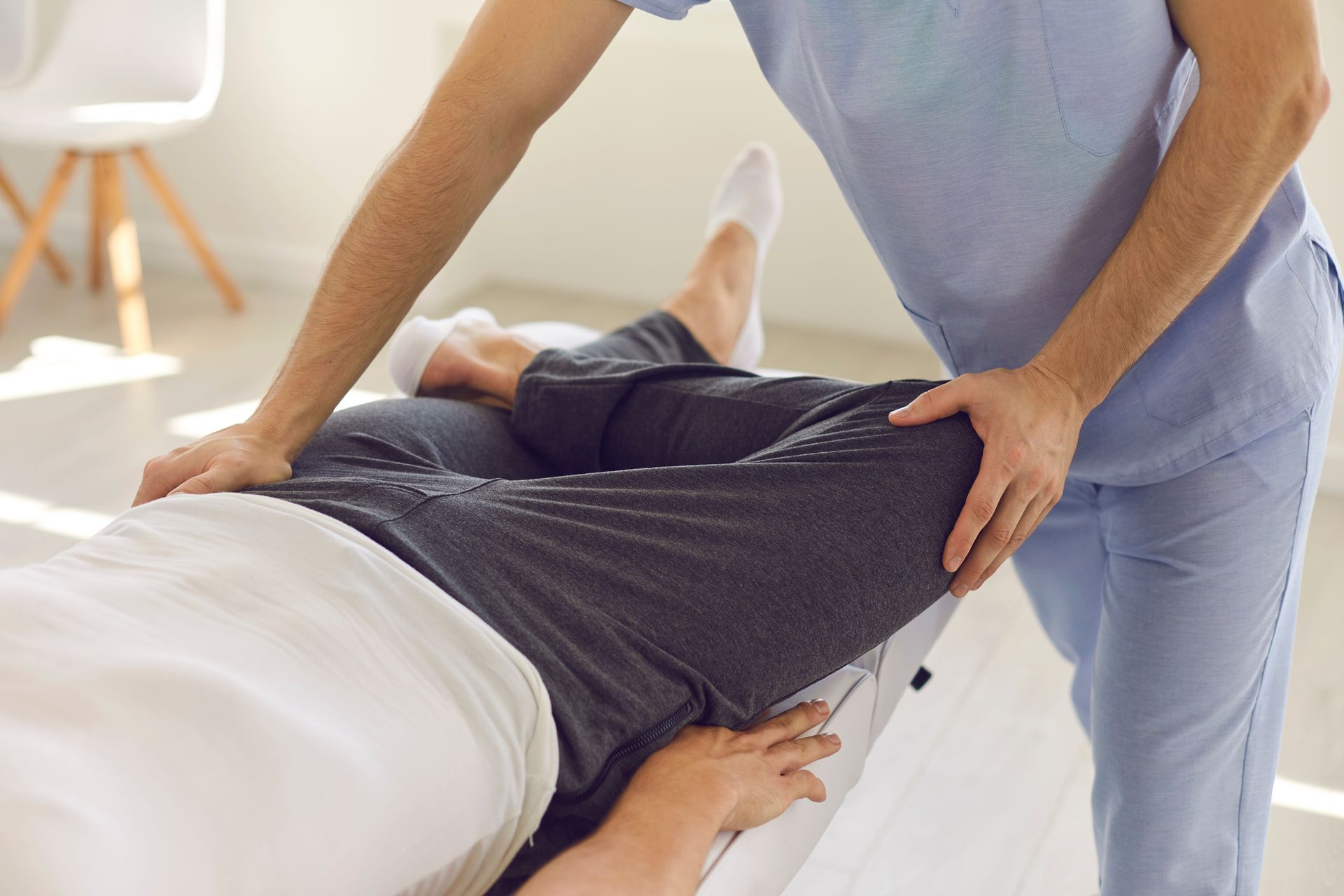 Un thérapeute en blouse bleu clair effectue un étirement des jambes sur un patient allongé sur une table de traitement.