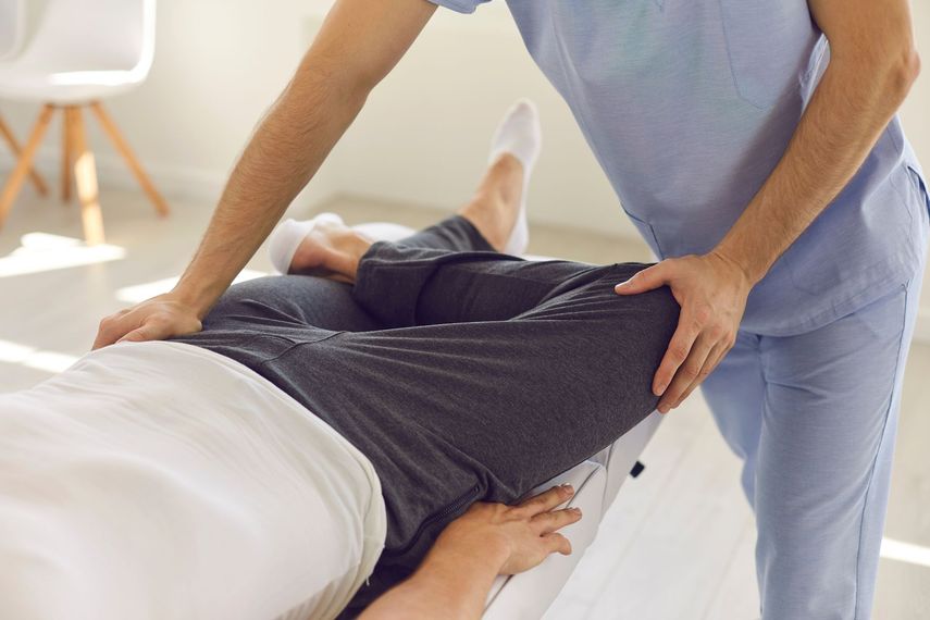 Un thérapeute en blouse bleu clair effectue un étirement des jambes sur un patient allongé sur une table de traitement.