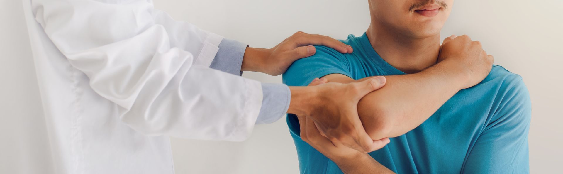 Un professionnel de santé en blouse blanche effectue un examen physique de l'épaule d'un patient.