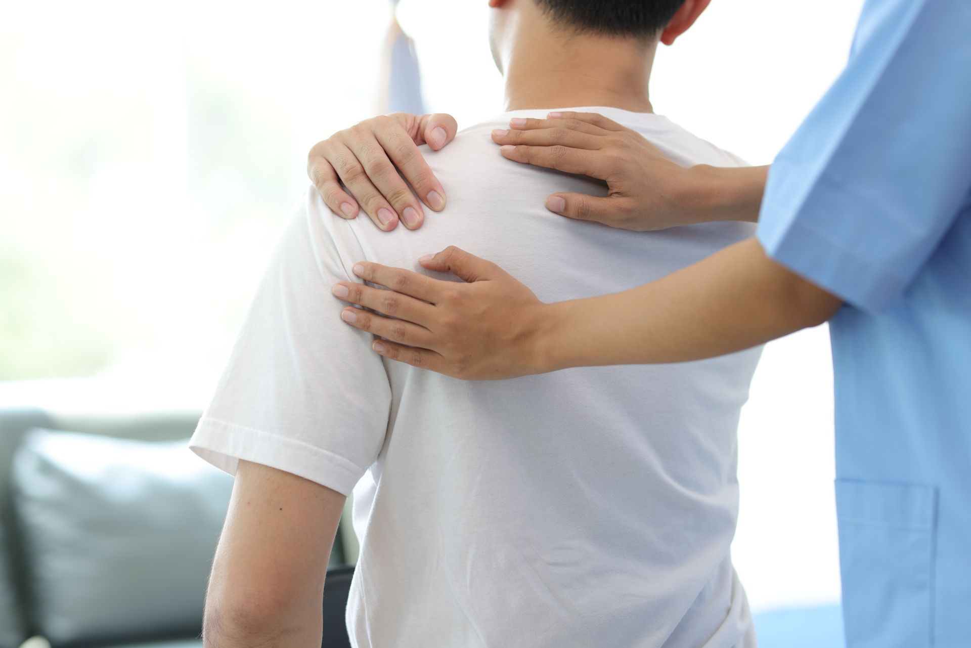 Un professionnel de santé en blouse bleue effectue un examen physique de l'épaule d'un patient.
