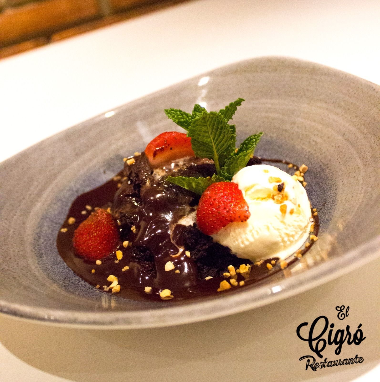 Postre en un cuenco gris con salsa de chocolate, fresas, menta y una bola de helado de vainilla