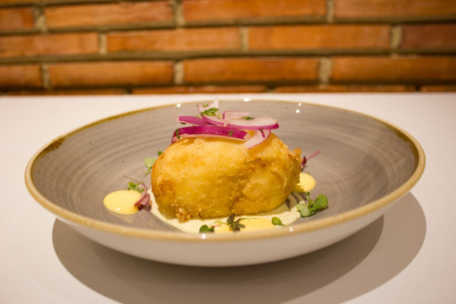 Plato gourmet emplatado con cebolla roja por encima, servido en un plato blanco en un restaurante