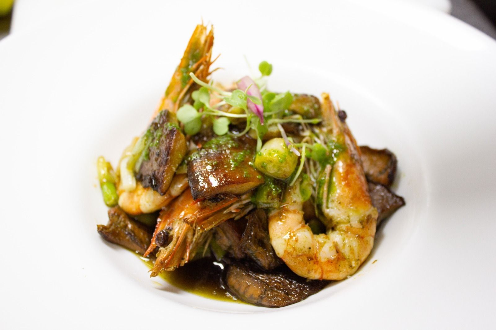 Gambas y champiñones emplatados, decorados con microvegetales, sobre un plato blanco