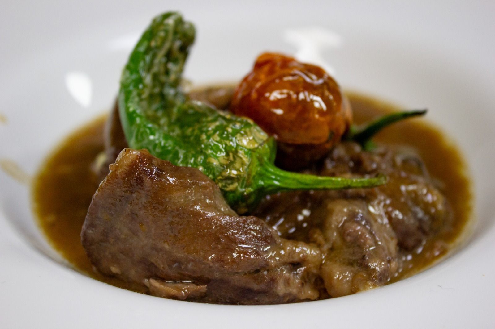 Carne estofada emplatada con salsa marrón, pimientos verdes y guarnición de tomate asado