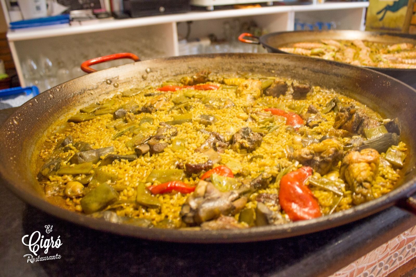 Una gran sartén de arroz amarillo con carne y pimientos rojos, cocinándose a fuego lento en una cocina durante un bufé.