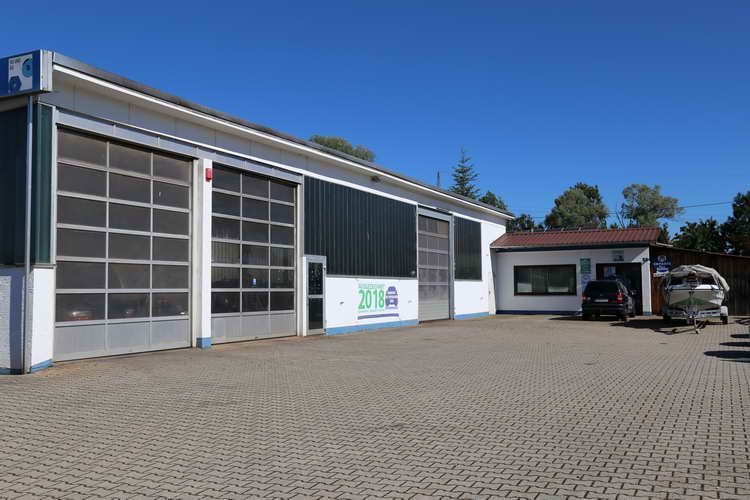 Garage mit drei großen Toren, ein seitliches Büro und ein gepflasterter Parkplatz unter strahlend blauem Himmel.