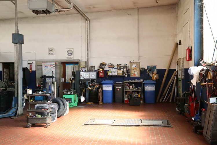 Innenansicht einer Autowerkstatt. Werkzeuge, Ausrüstung und eine Hebebühne sind zu sehen. Weiße Wände, roter Fliesenboden.