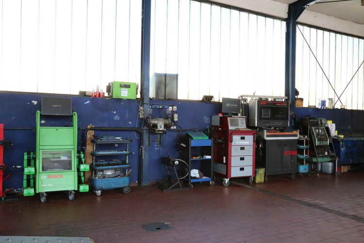 Das Innere einer Autowerkstatt mit mehreren Werkzeugwagen und Diagnosegeräten vor einer blauen Wand.