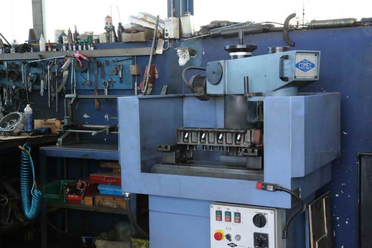 Blaue Werkzeugmaschine in einer Werkstatt, vermutlich für Motoreninstandsetzung. Werkzeuge und Werkbank sind im Hintergrund zu sehen.