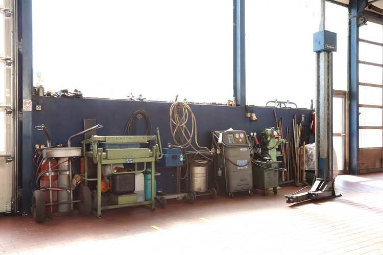 Werkzeuge und Ausrüstung in einer Autowerkstatt, darunter eine Hebebühne, Schweißzubehör und Transportwagen.