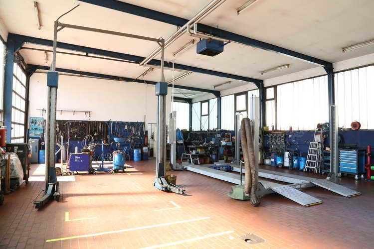 Innenansicht einer gut beleuchteten Autowerkstatt mit Hebebühnen, Werkzeugen und Ausrüstung.