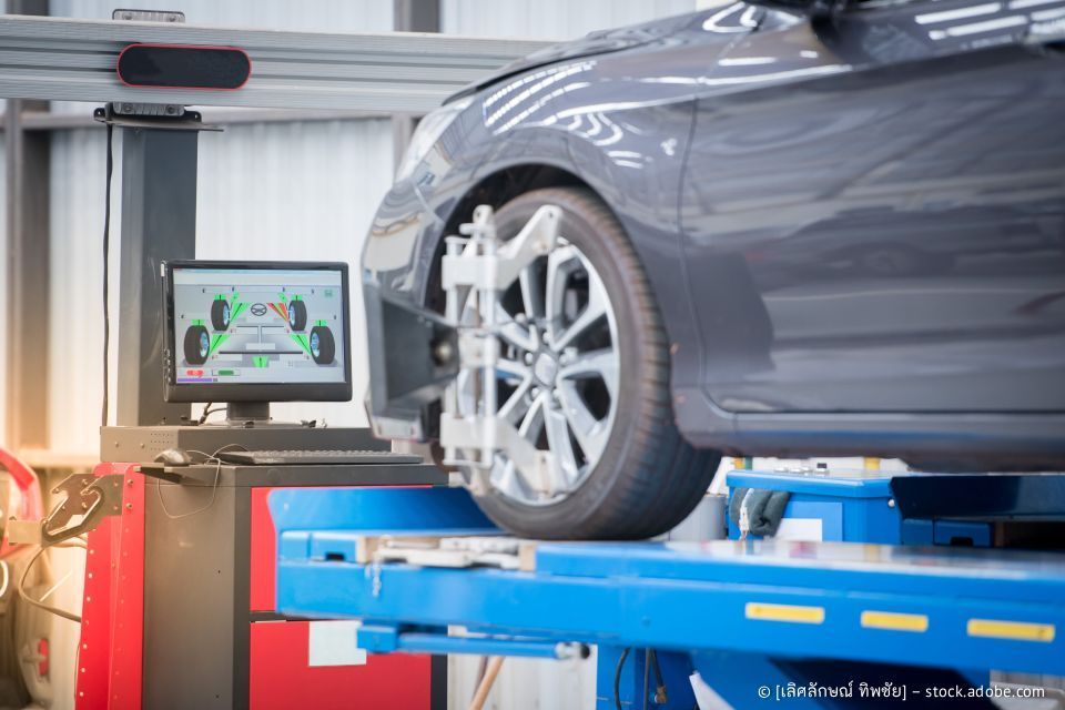 Ein Auto steht auf einer Hebebühne in einer Werkstatt und wird vermessen. Der Computerbildschirm zeigt die Messwerte an.