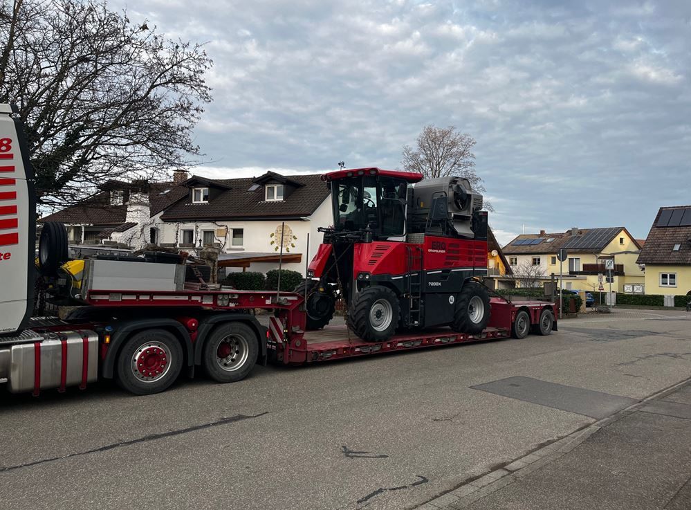Ein rot-schwarzer Traktor wird auf einem Anhänger transportiert.