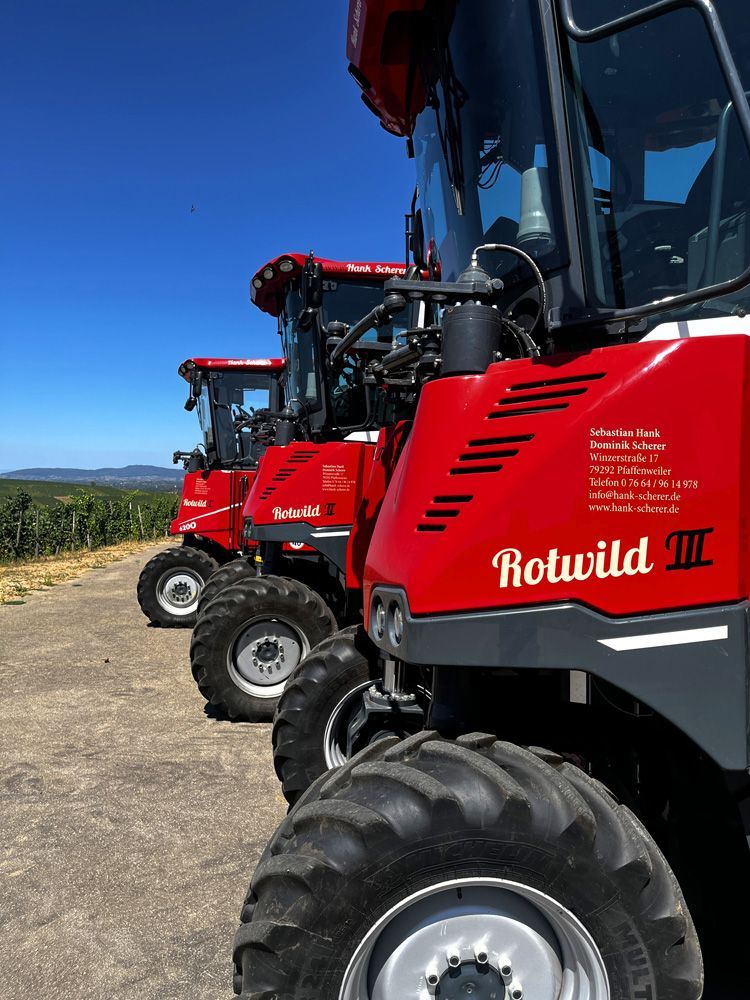 Eine Reihe roter Rotwild-Mähdrescher parkt neben einem Feld unter klarem, blauem Himmel