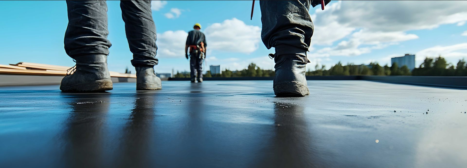 Deux ouvriers en bottes traversent un toit plat et sombre en direction d'un troisième ouvrier.