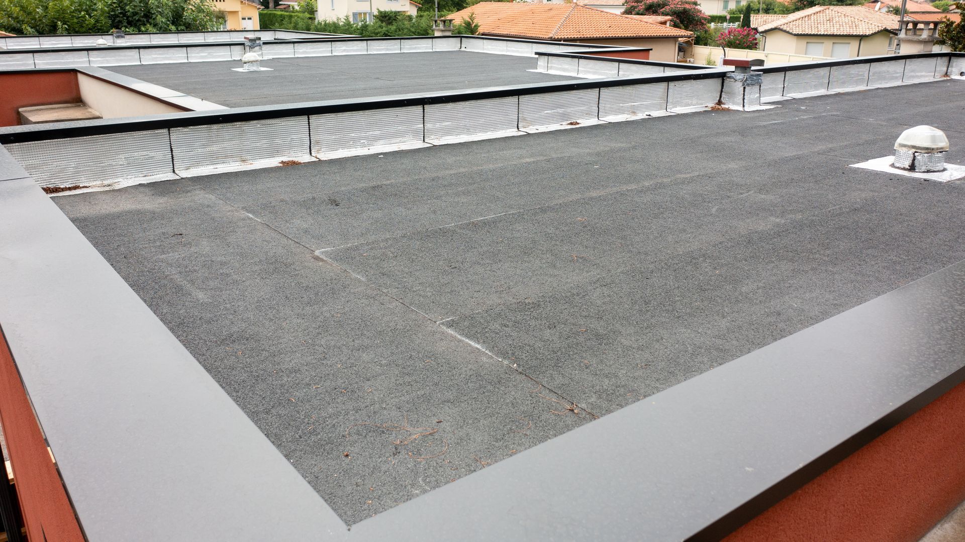 Un toit plat recouvert de gravier foncé, bordé d'une bande de métal gris lisse, se détachant sur un fond flou.