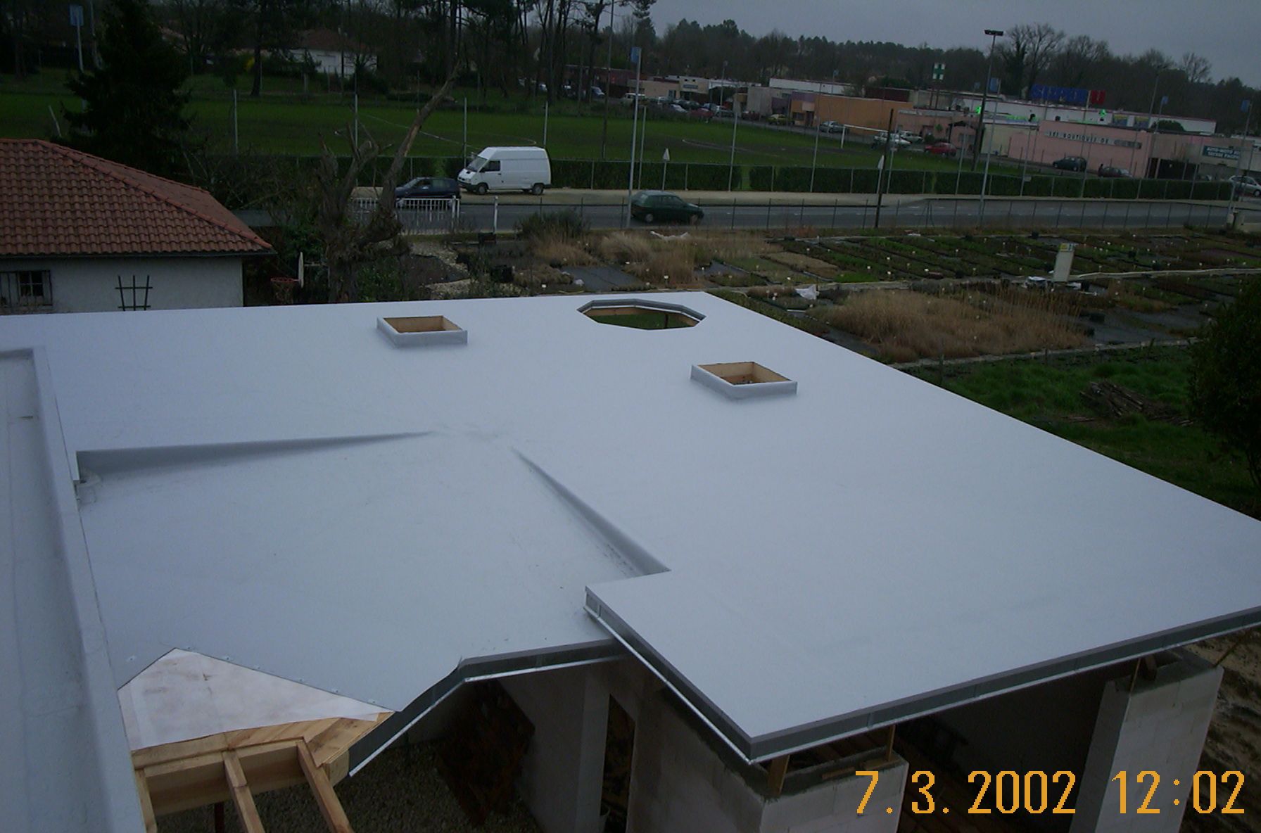 Un ouvrier portant un équipement de protection utilise une torche pour installer un revêtement de toiture.
