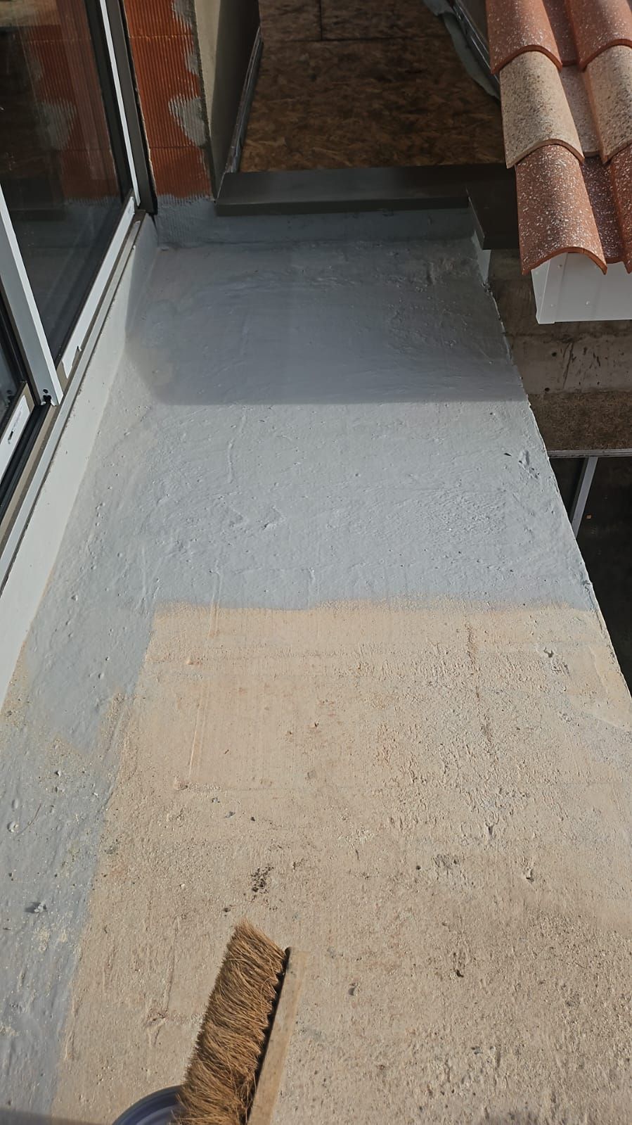 Un ouvrier en tenue de travail bleue utilise un rouleau à long manche pour appliquer un mastic liquide.