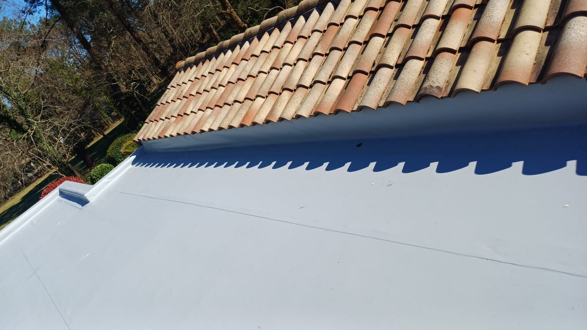 Un toit de tuiles, montrant une partie propre et orange à gauche et une partie sale et sombre à droite.