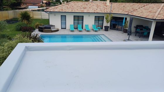 Des ouvriers utilisent un chalumeau pour installer un rouleau de matériau de toiture noir sur une surface plane.