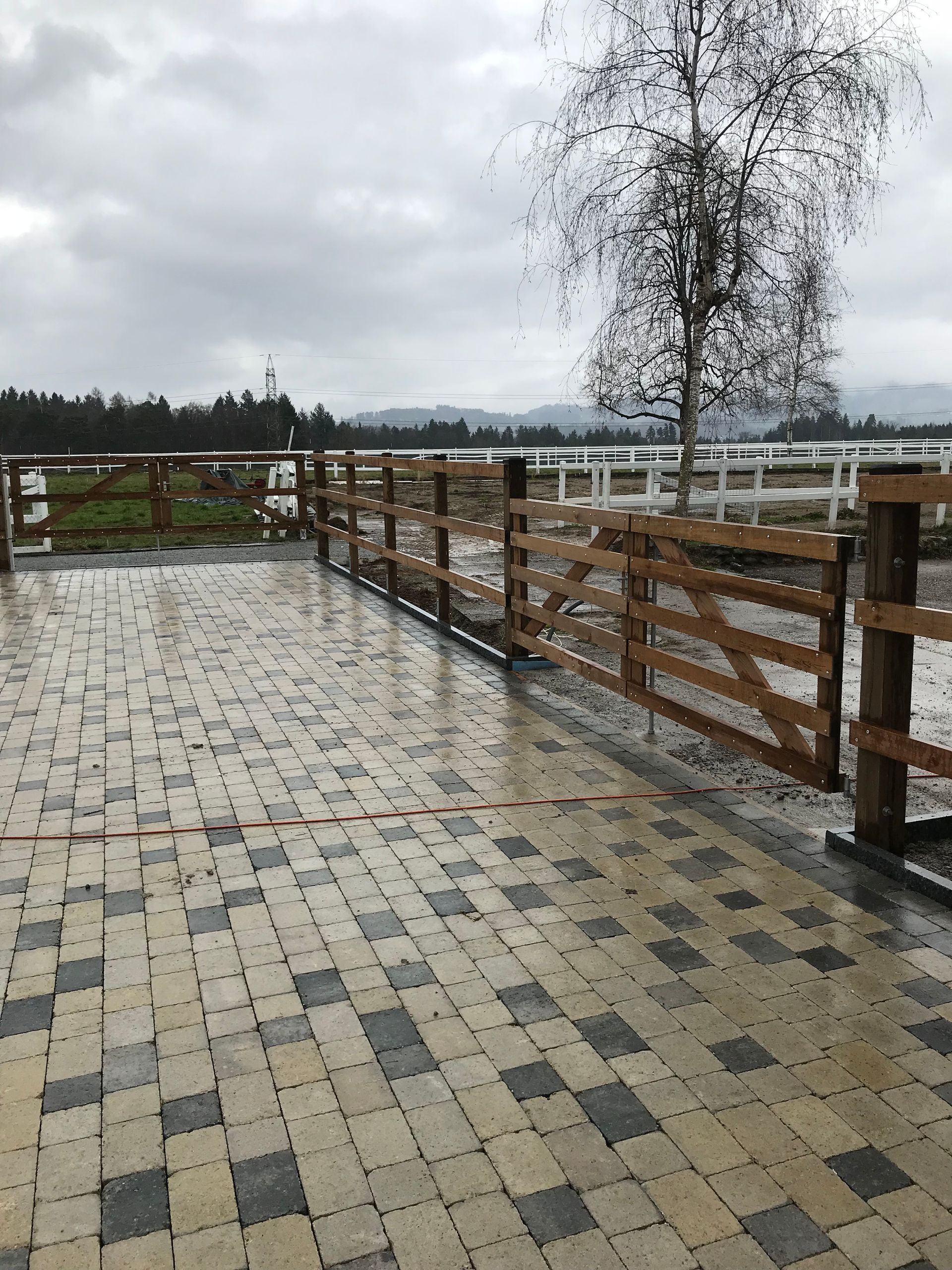 Ein gemauerter Gehweg mit einem Holzzaun und einem Baum im Hintergrund