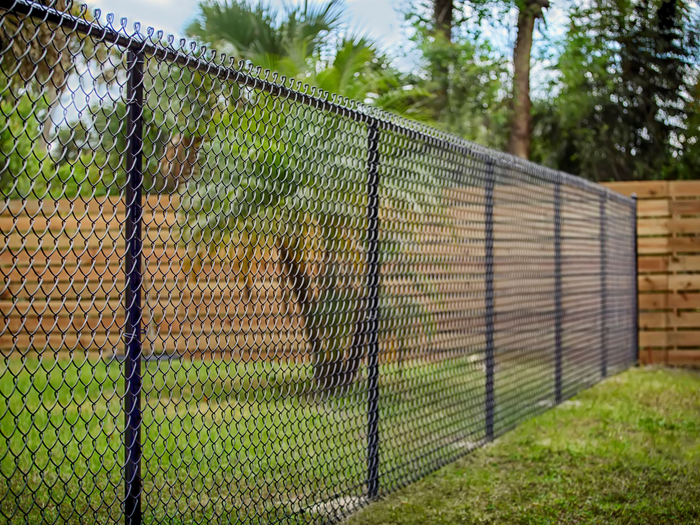 Clôture en grillage noir le long d’un jardin gazonné, avec une palissade en bois en arrière-plan