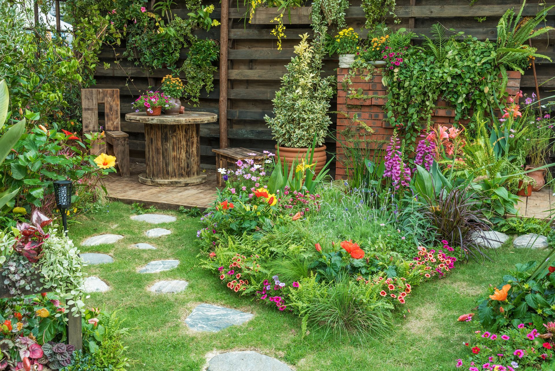 Jardin de cottage luxuriant, parsemé de fleurs colorées, avec un chemin de pierre et un banc rustique en bois près d’un mur de briques
