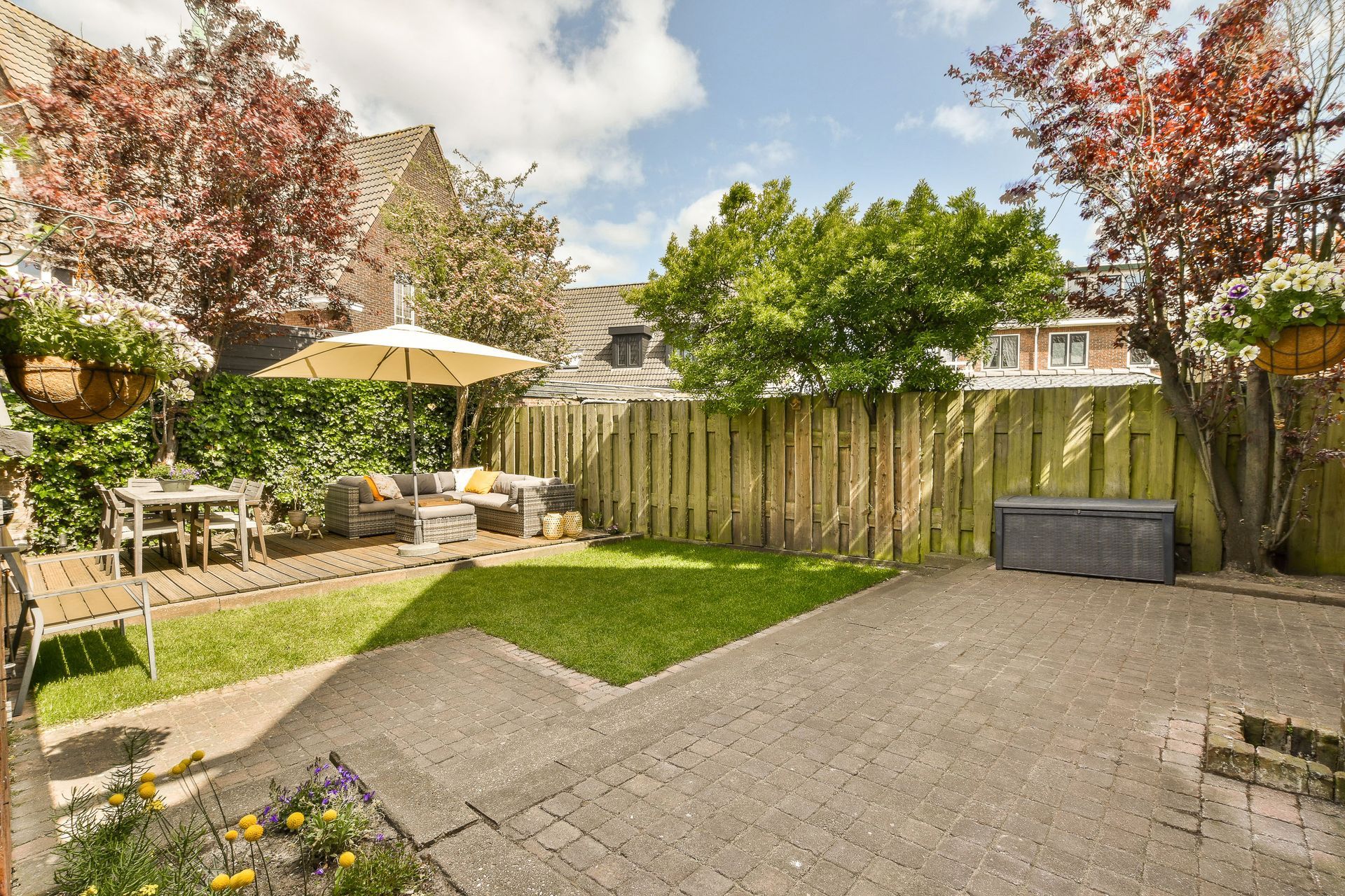 Patio dans le jardin avec sol en gravier, clôture en bois, coin repas avec parasol et arbres verts baignés par la lumière automnale
