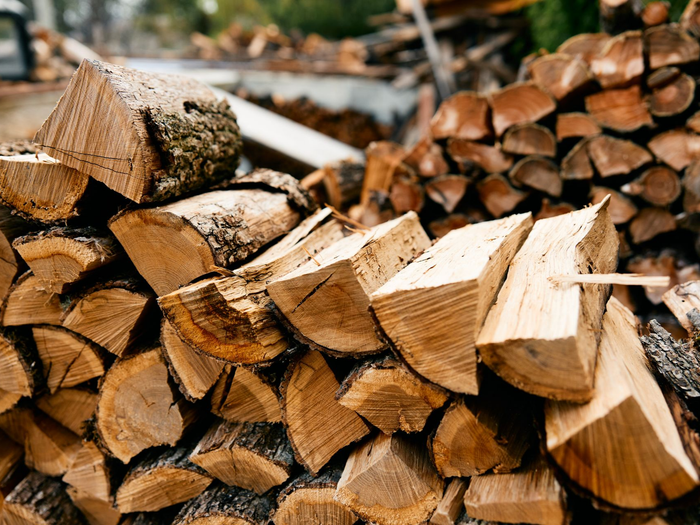 Bûches de bois de chauffage empilées à l’extérieur, les extrémités coupées tournées vers l’avant et d’autres bûches floues en arrière-plan