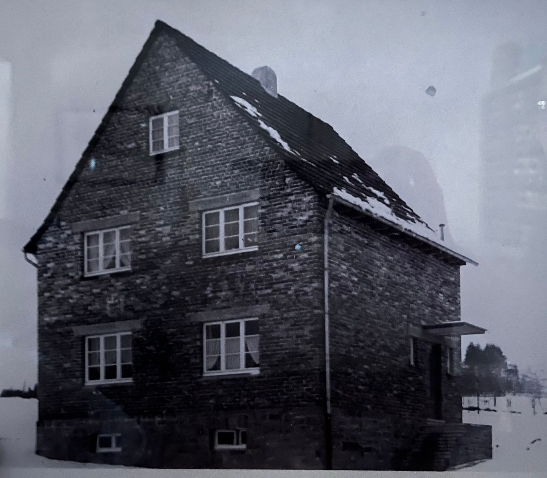 Backsteinhaus mit Schnee auf dem Dach und dem Boden, mehreren Fenstern, einem überdachten Eingang und einem Schornstein.