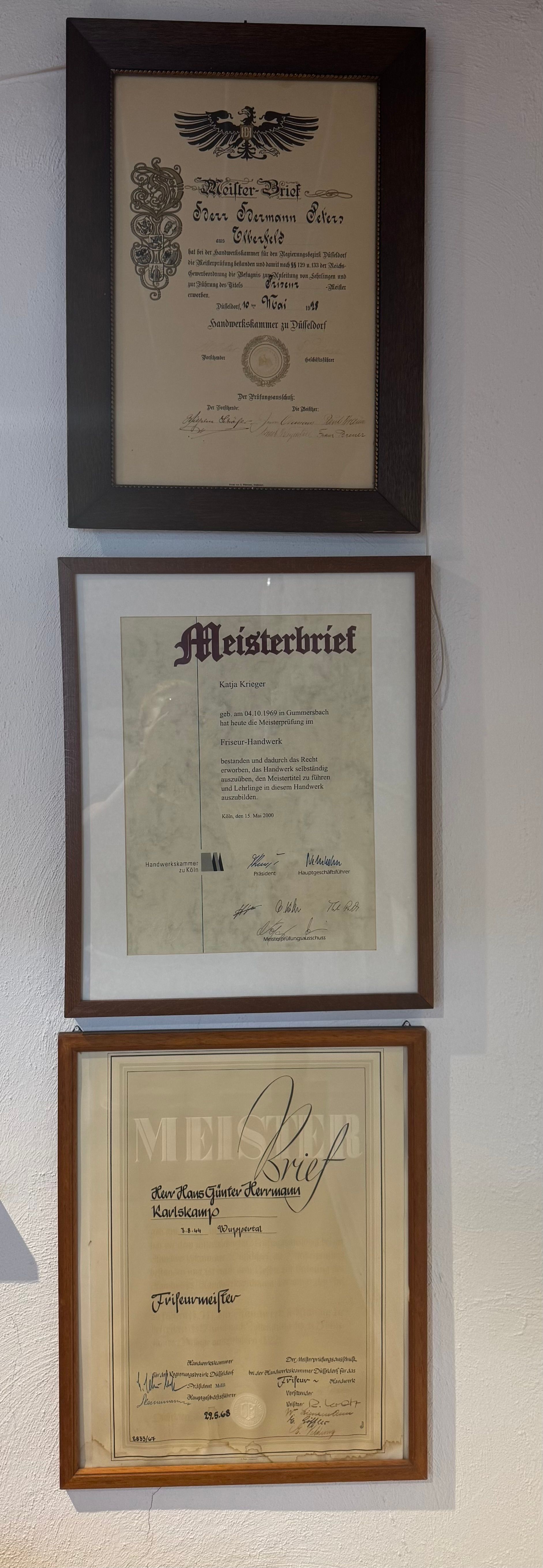 An einer weißen Wand hängen drei gerahmte Dokumente mit schwarzem Text auf gealtertem Papier.
