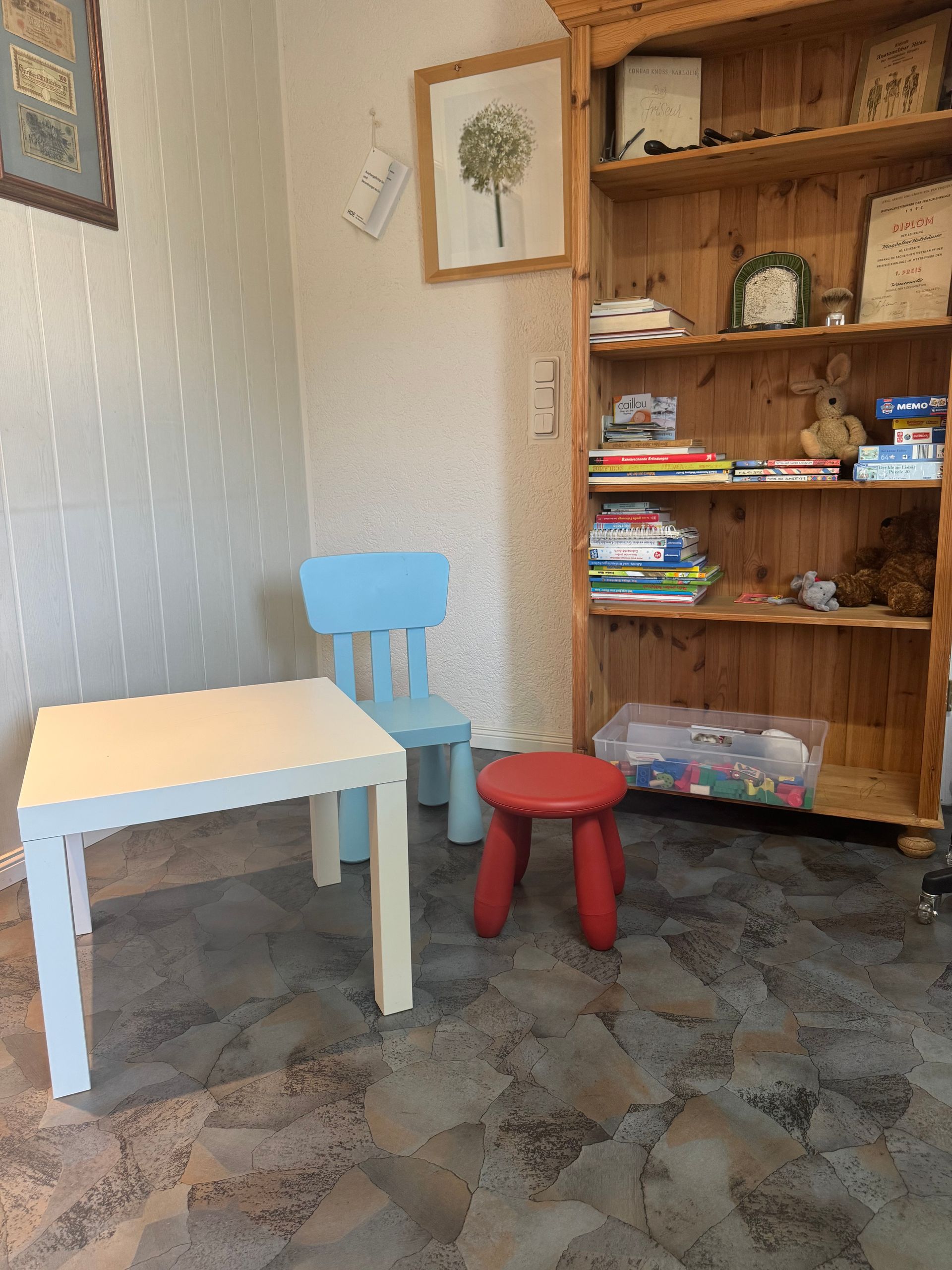 Ein Kinderspielbereich mit einem Tisch, Stühlen und einem Bücherregal voller Spielsachen und Bücher.