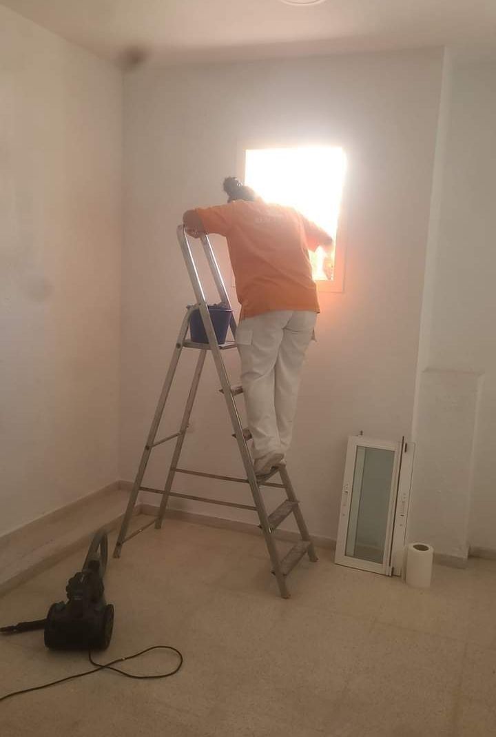 Un hombre está de pie en una escalera en una habitación pintando una ventana.