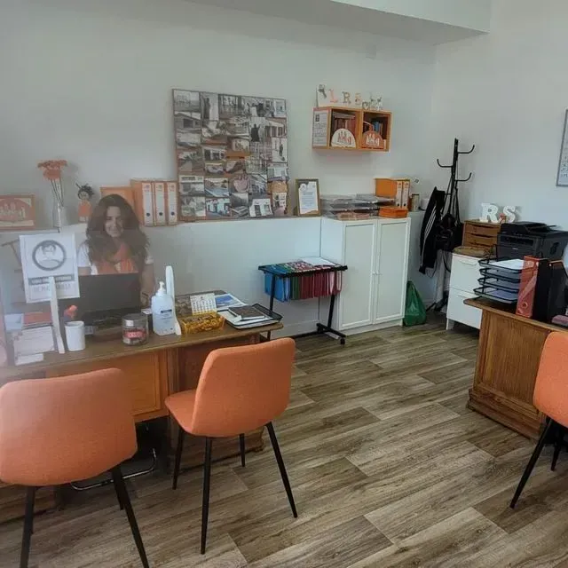 Una mujer está sentada en un escritorio en una oficina con sillas naranjas.