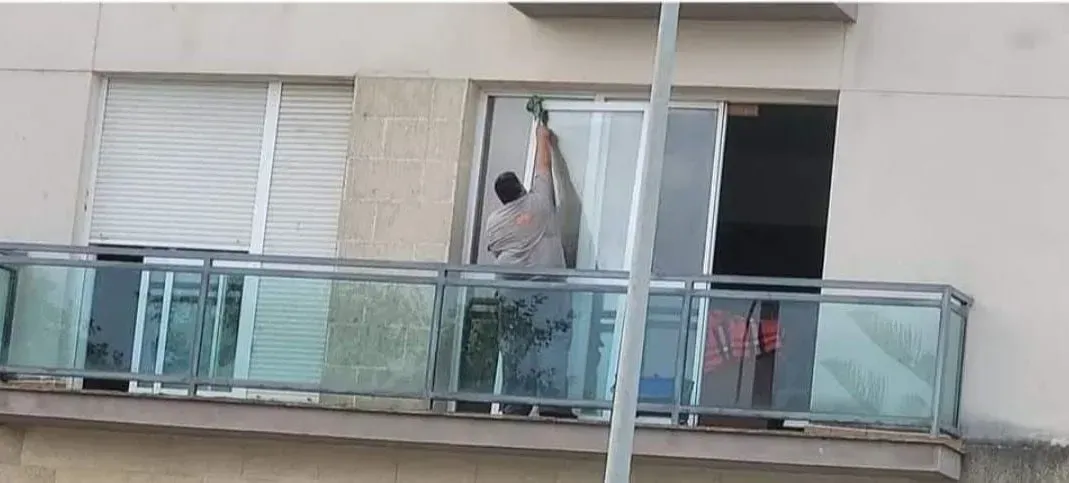 Un hombre está parado en un balcón limpiando una ventana.