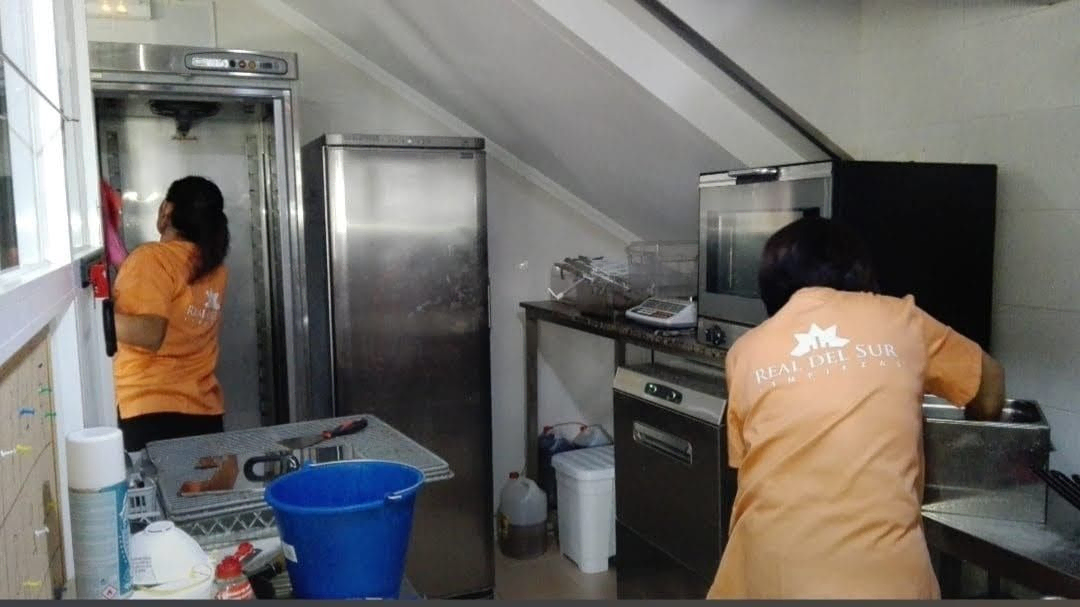 Una mujer con una camisa naranja está limpiando una cocina.