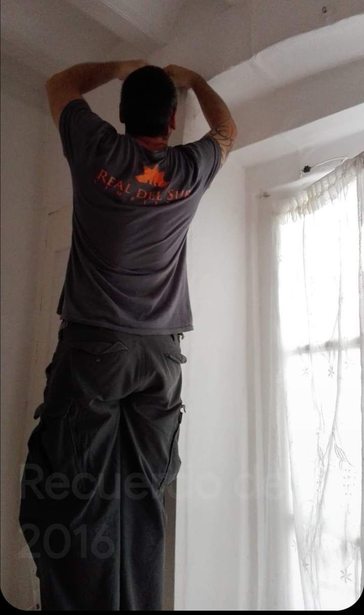 Un hombre con una camisa gris está de pie en una pared.