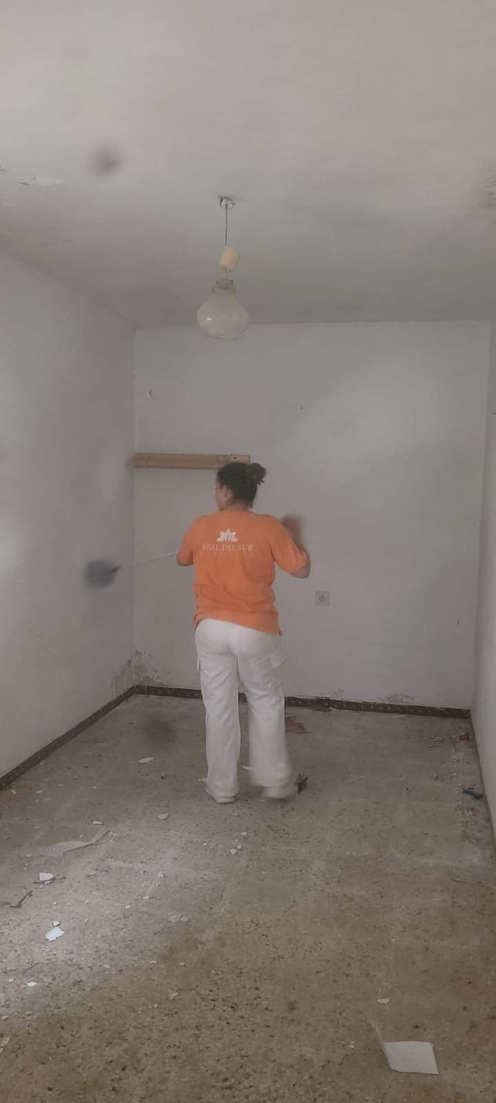 Un hombre está parado en una habitación vacía pintando una pared.
