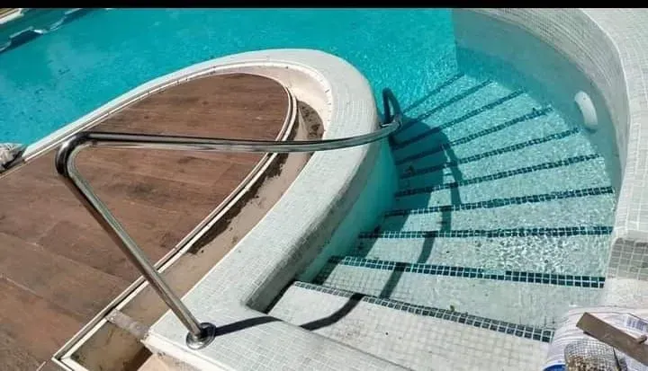 Una piscina con escaleras que conducen a ella y una barandilla de acero inoxidable.