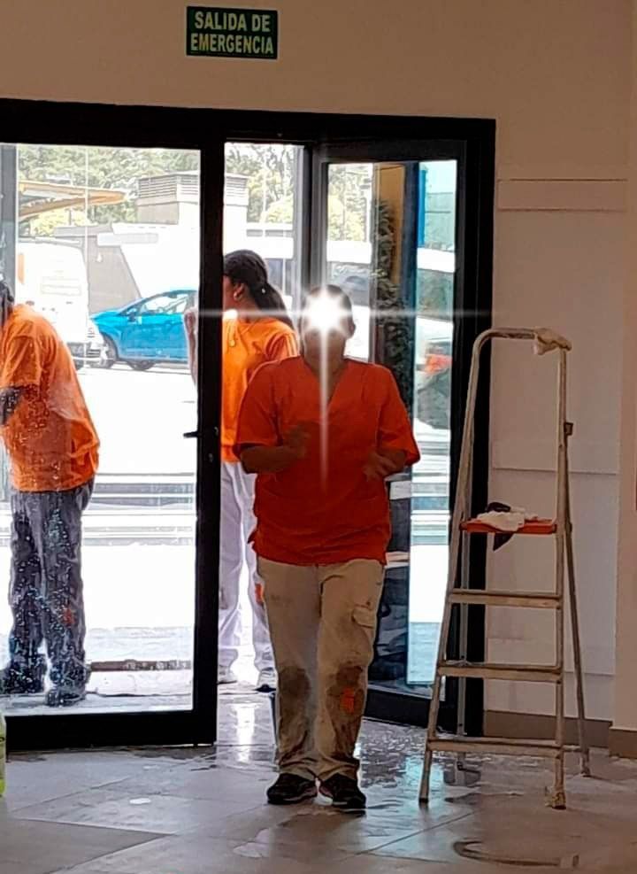 Un hombre con una camisa naranja está parado frente a una puerta de vidrio.